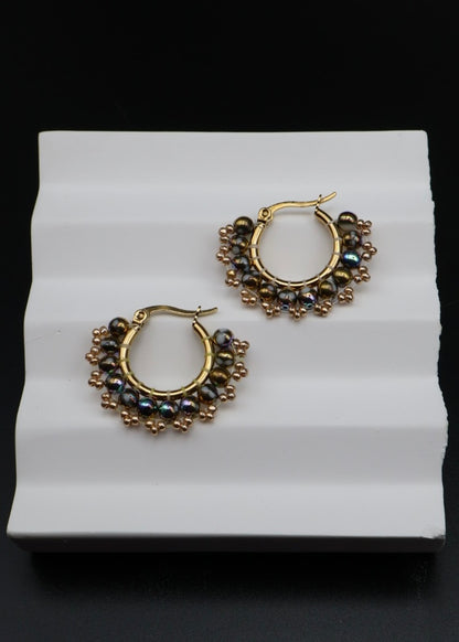 Gold hoop earrings with black beads on a white stand against a black background