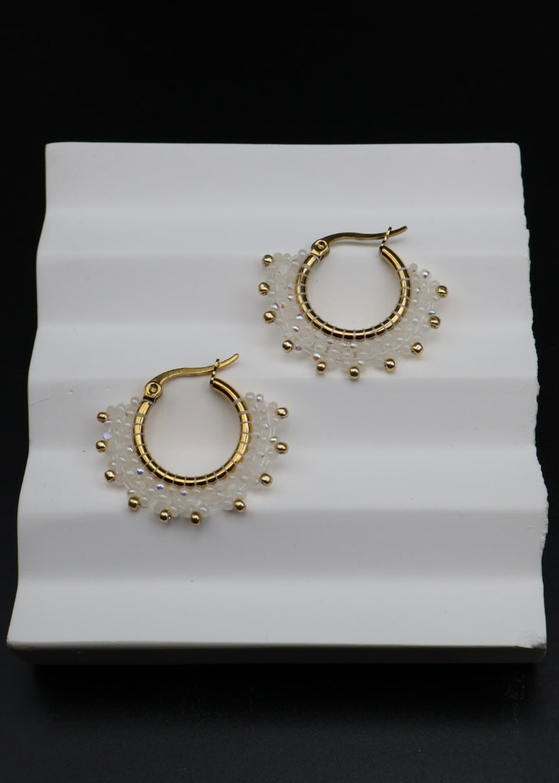 Pair of gold hoop earrings with bead detailing on a white stand.