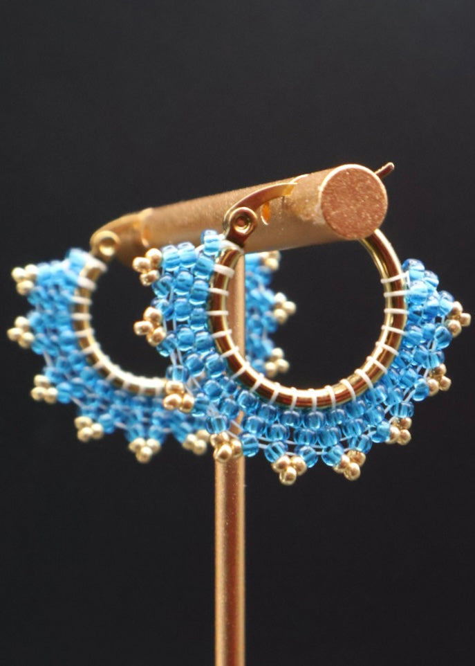 Gold hoop earrings with blue beaded accents on a black background