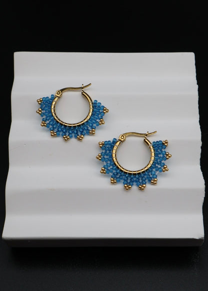 Pair of gold hoop earrings with blue beads on a white stand against a black background