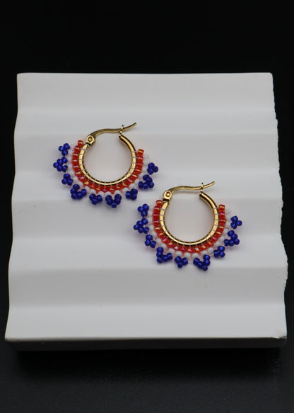 Pair of hoop earrings with blue and red beads on a white stand.