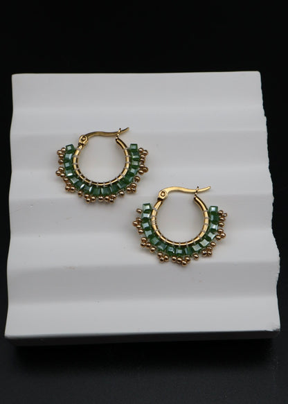 Gold hoop earrings with green gemstones on a white surface