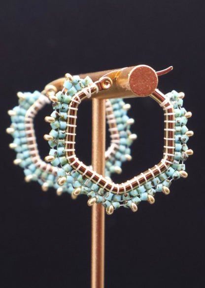 Turquoise beaded hoop earrings on a stand against a black background