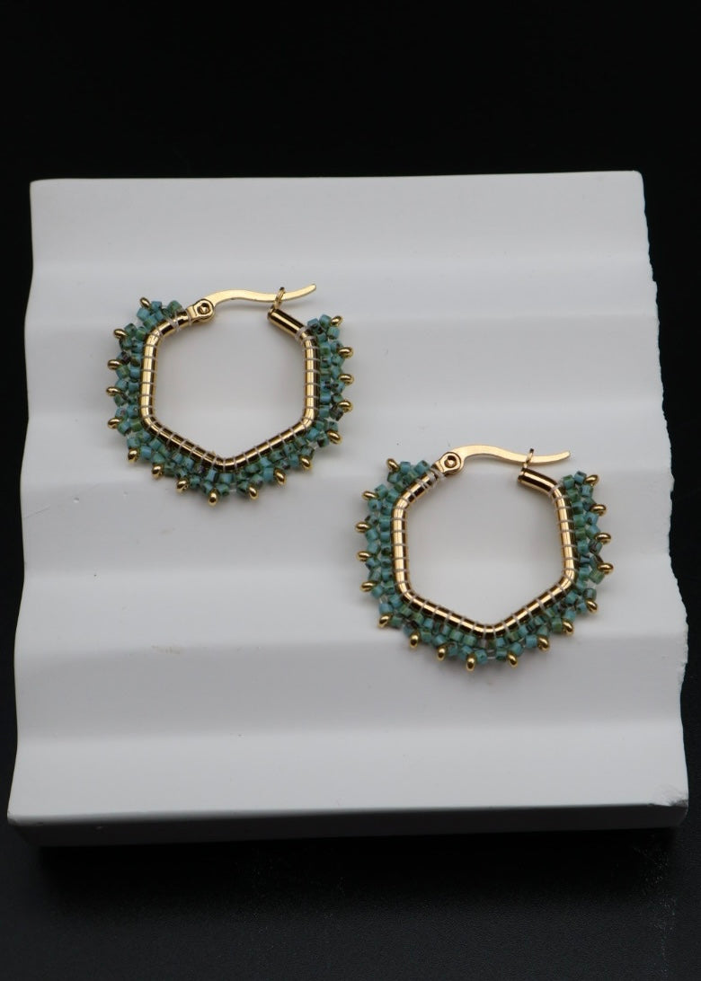 Hexagonal hoop earrings with gold and green beads on a white stand.