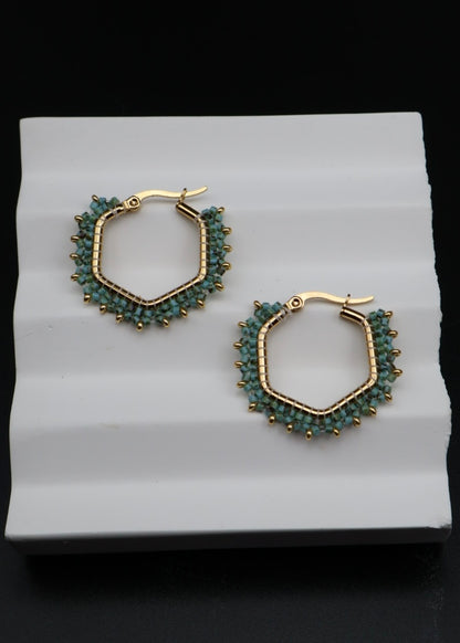 Hexagonal hoop earrings with gold and green beads on a white stand.