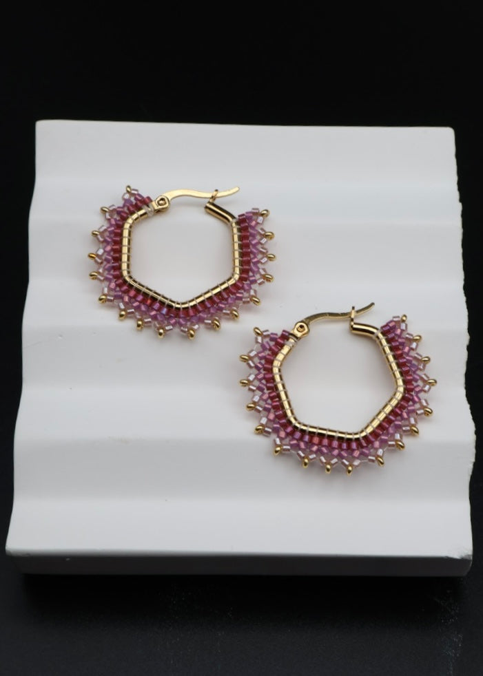 Pair of gold hoop earrings with pink gemstones on a white stand against a black background