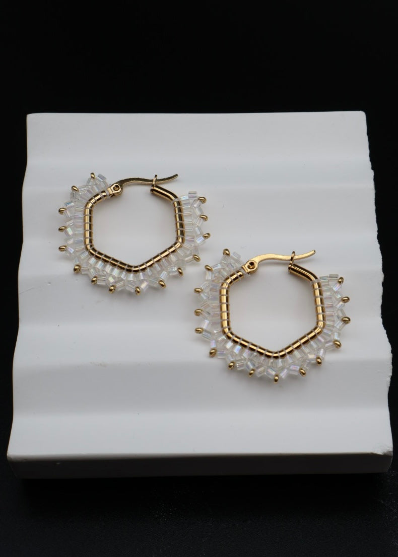 Hexagonal hoop earrings with gold and pearl detailing on a white stand.