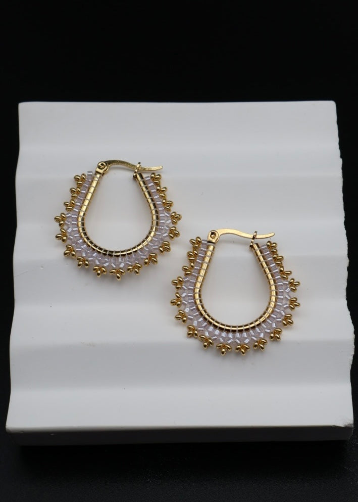 Gold hoop earrings with bead detailing on a white stand against a black background