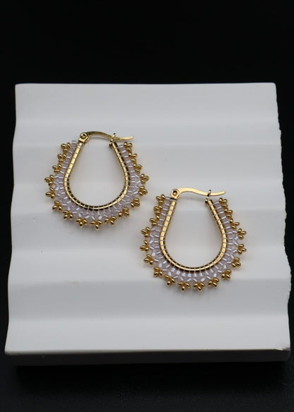 Gold hoop earrings with bead detailing on a white stand against a black background