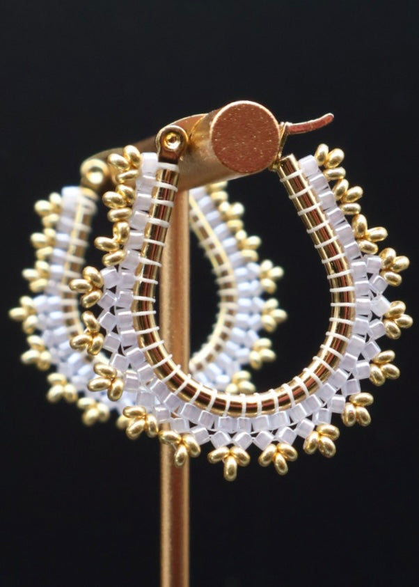 Gold and white beaded hoop earrings on a black background