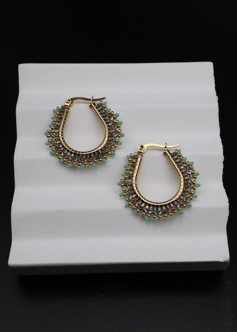Pair of gold and green hoop earrings on a white stand with a black background