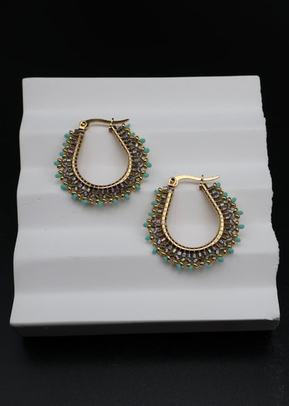Pair of gold and green hoop earrings on a white stand with a black background
