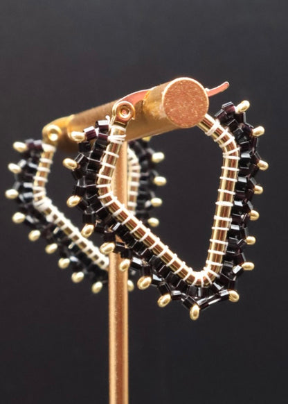 Gold hoop earrings with black gemstones on a stand against a dark background