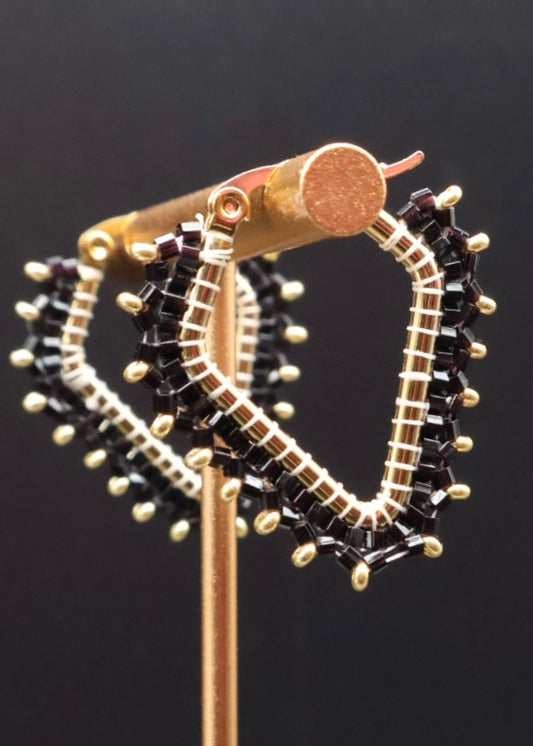 Gold hoop earrings with black gemstones on a stand against a dark background