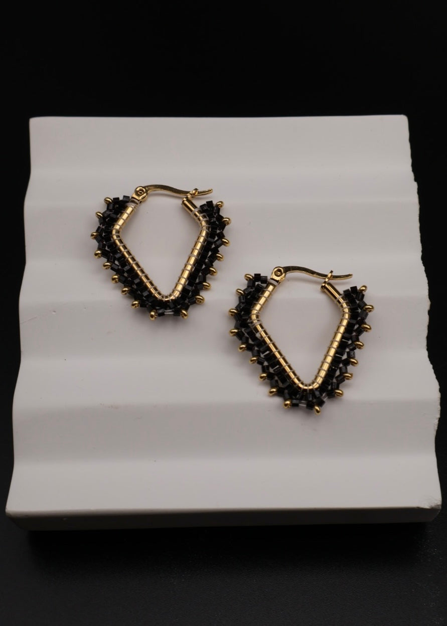 Gold and black hoop earrings on a white stand with a black background