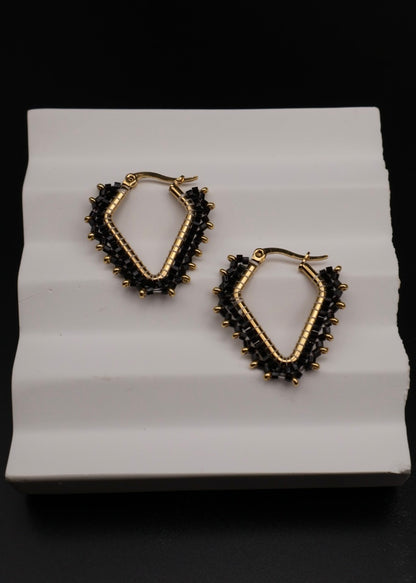 Gold and black hoop earrings on a white stand with a black background
