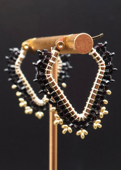 Gold and black beaded hoop earrings on a stand against a dark background