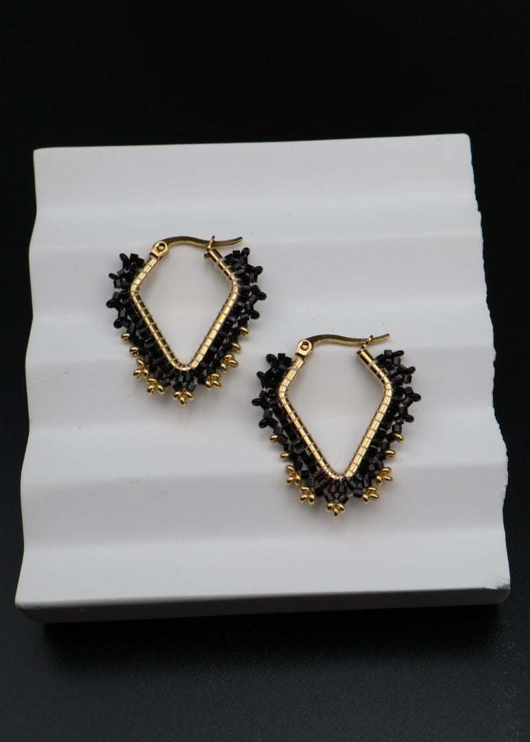Pair of gold and black hoop earrings on a white stand with a black background