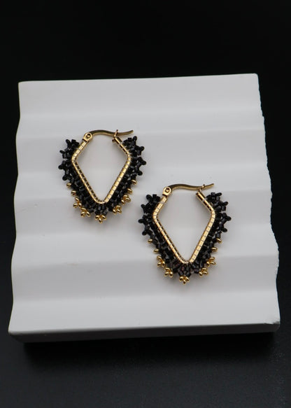 Pair of gold and black hoop earrings on a white stand with a black background