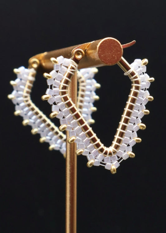 Gold and white beaded hoop earrings on a black background