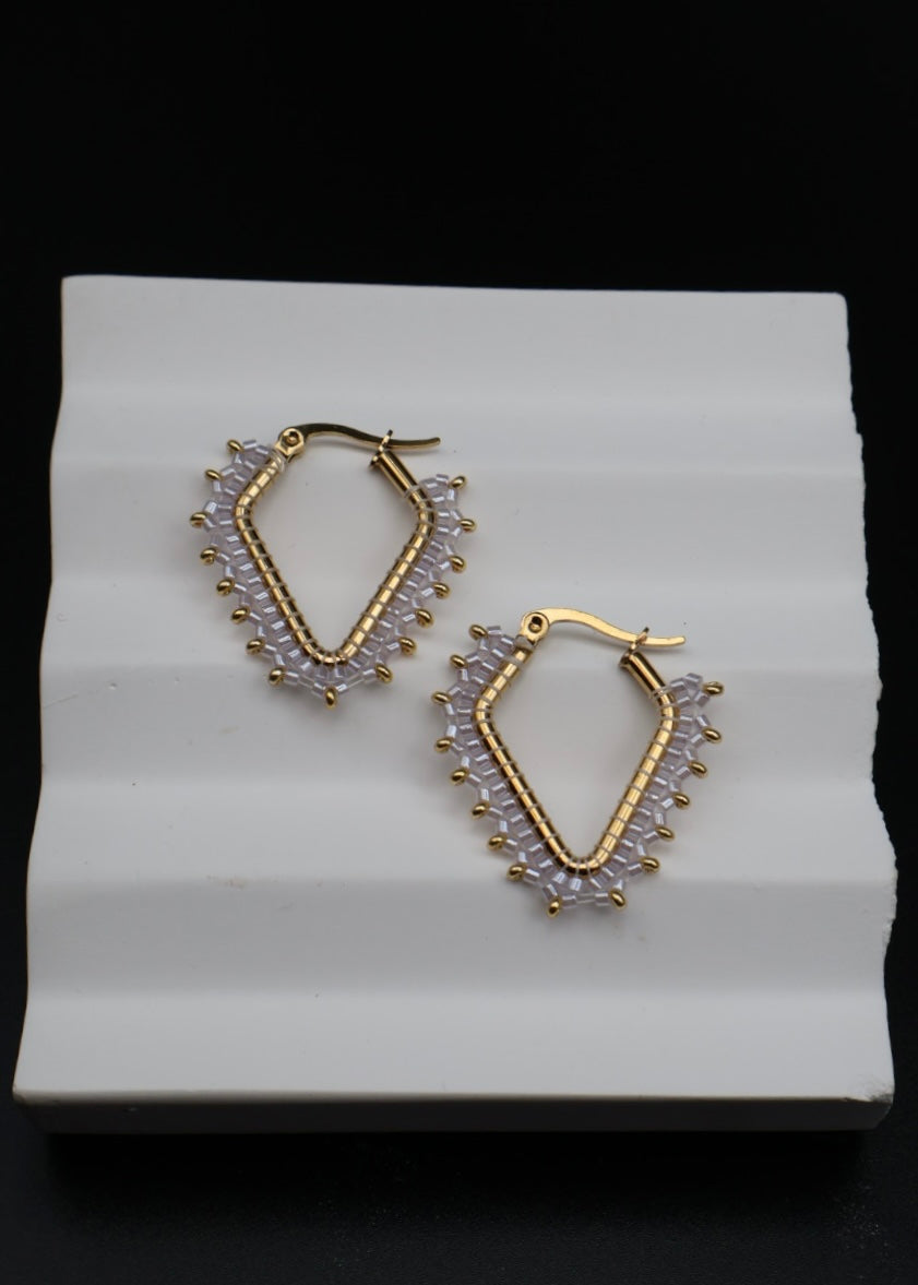 Gold hoop earrings with clear gemstones on a white textured surface