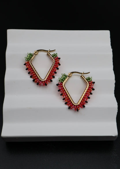 Pair of hoop earrings with red, green, and black stones on a white stand.