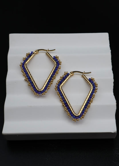Gold and blue hoop earrings on a white stand with a black background