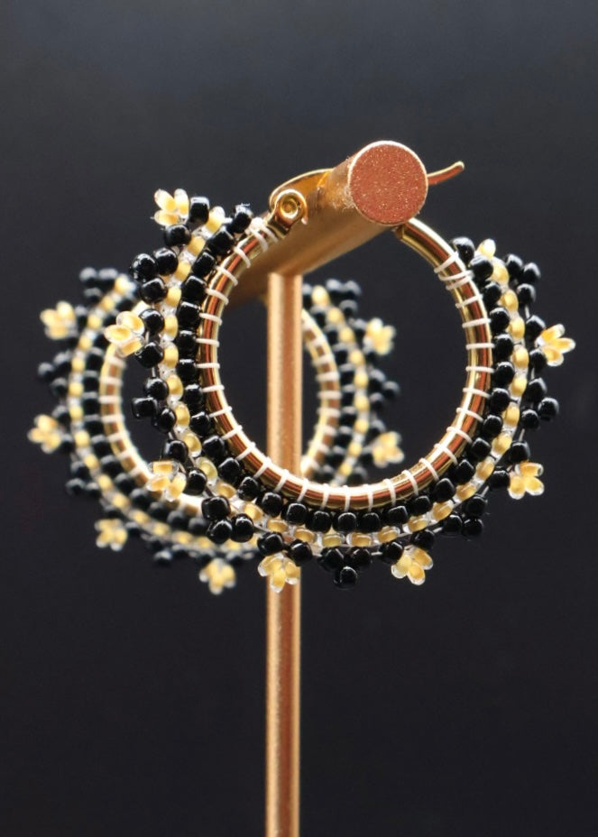 Gold and black beaded hoop earrings on a dark background