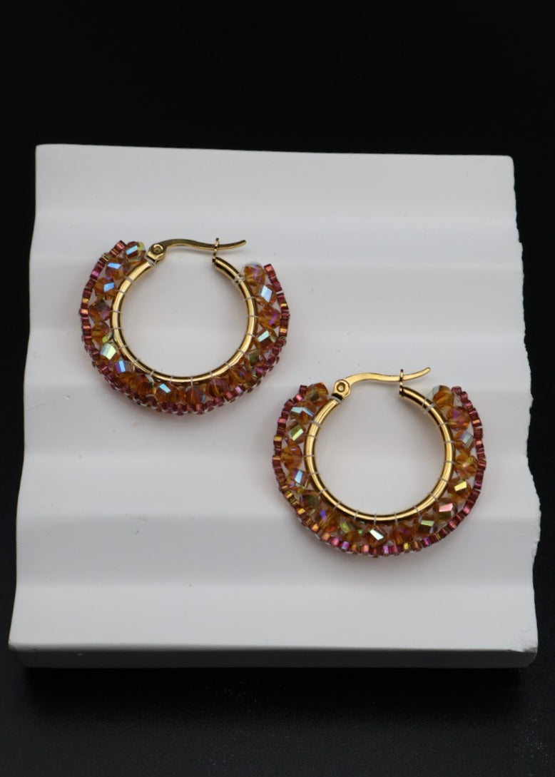 Gold hoop earrings with red gemstones on a white stand against a black background