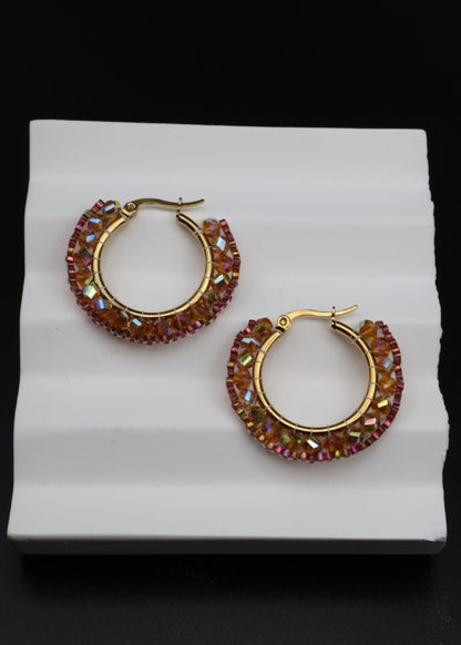 Gold hoop earrings with red gemstones on a white stand against a black background