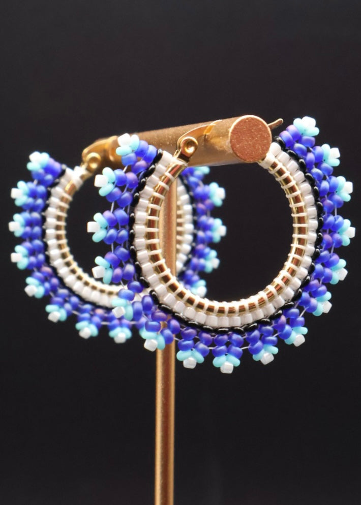 Blue and white beaded hoop earrings on a black background