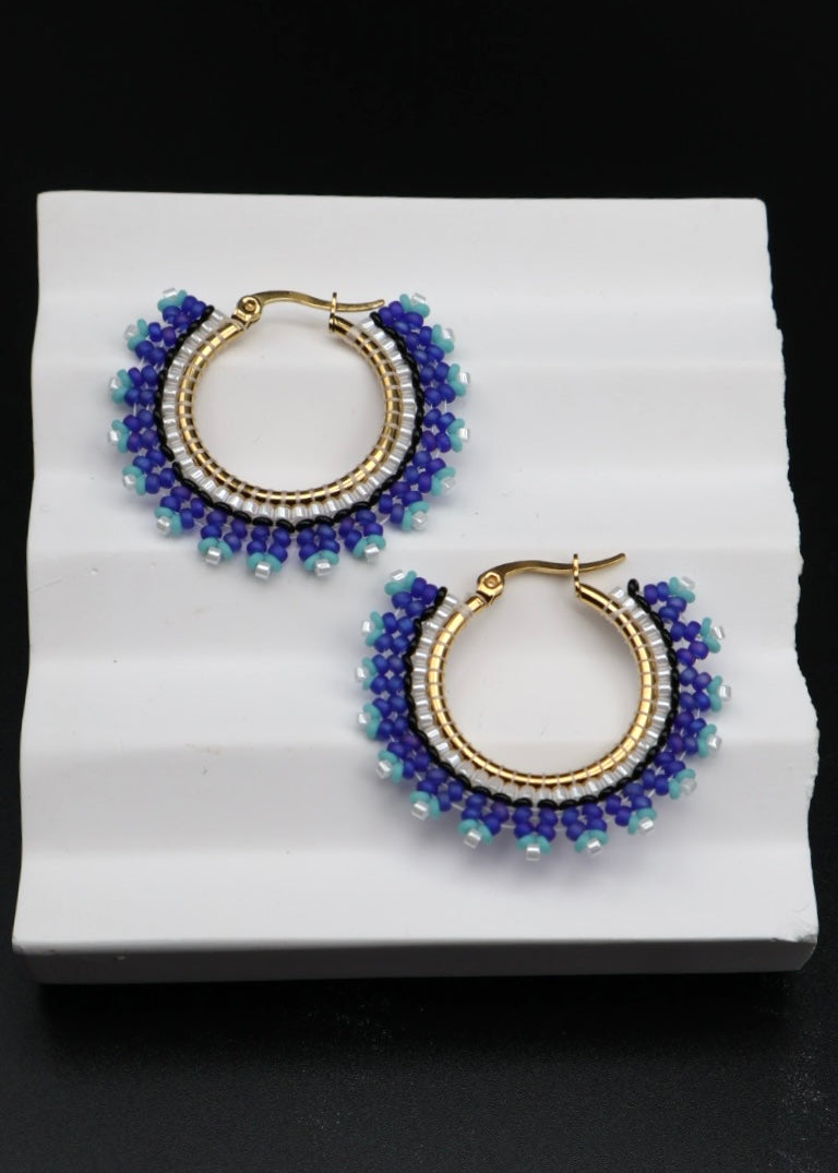 Pair of beaded hoop earrings on a white stand with a black background