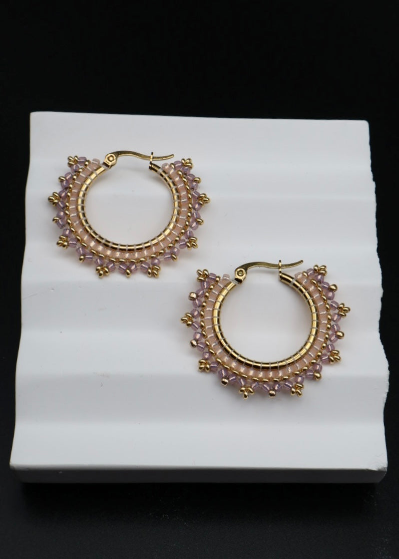 Gold hoop earrings with gemstones on a white stand against a black background