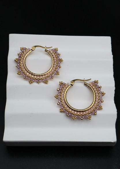 Gold hoop earrings with gemstones on a white stand against a black background
