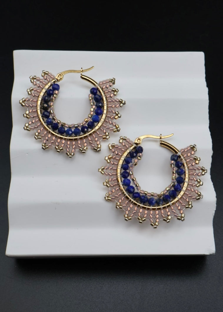 Gold hoop earrings with blue gemstones on a white stand against a black background
