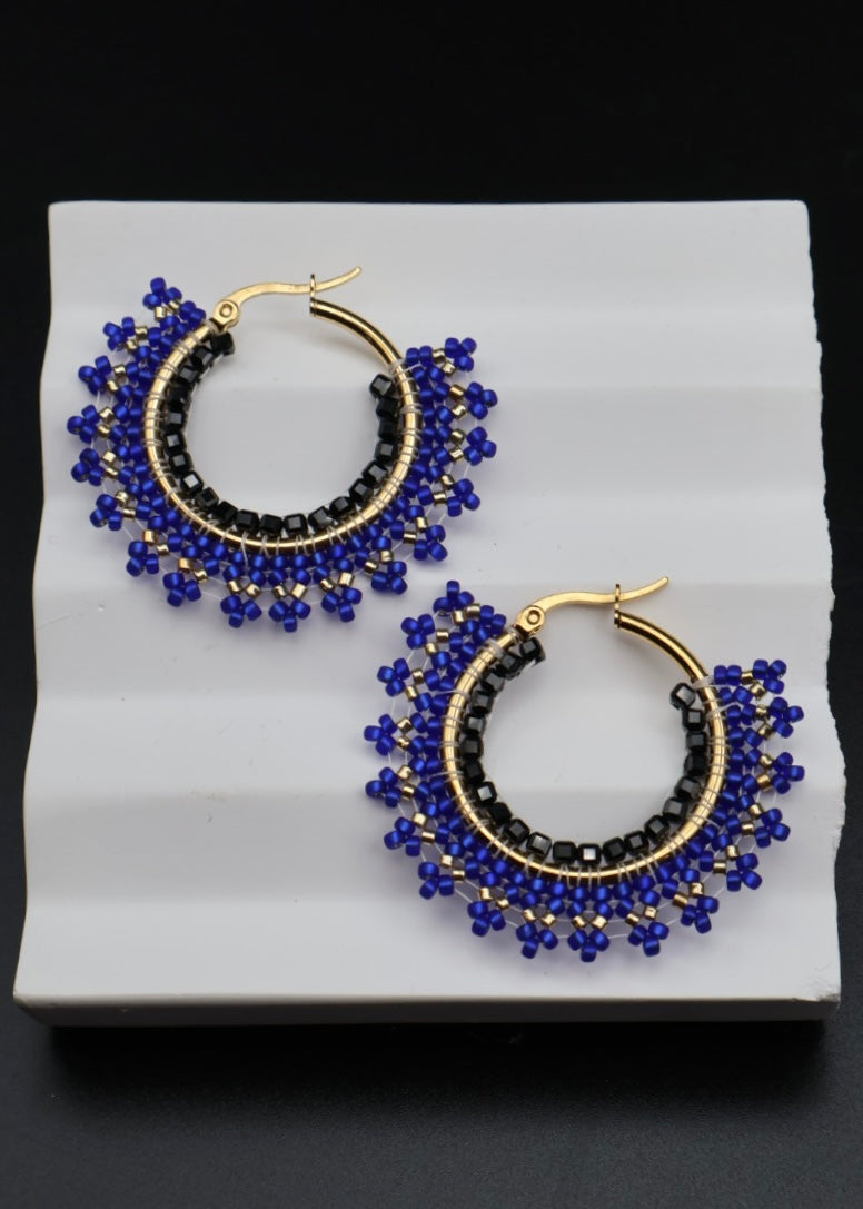 Pair of hoop earrings with blue and black beads on a white stand against a dark background