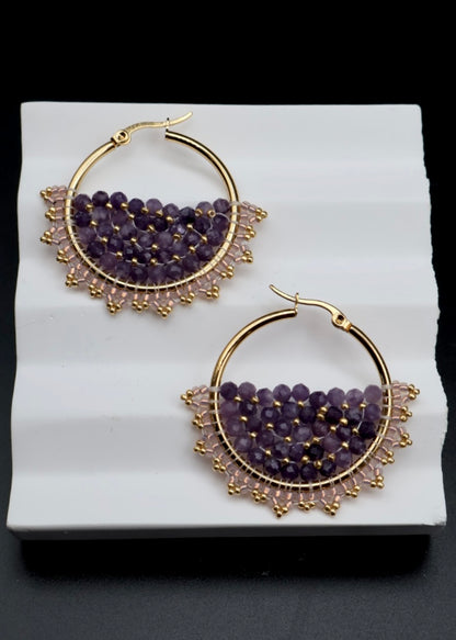 Gold hoop earrings with purple gemstones on a white surface