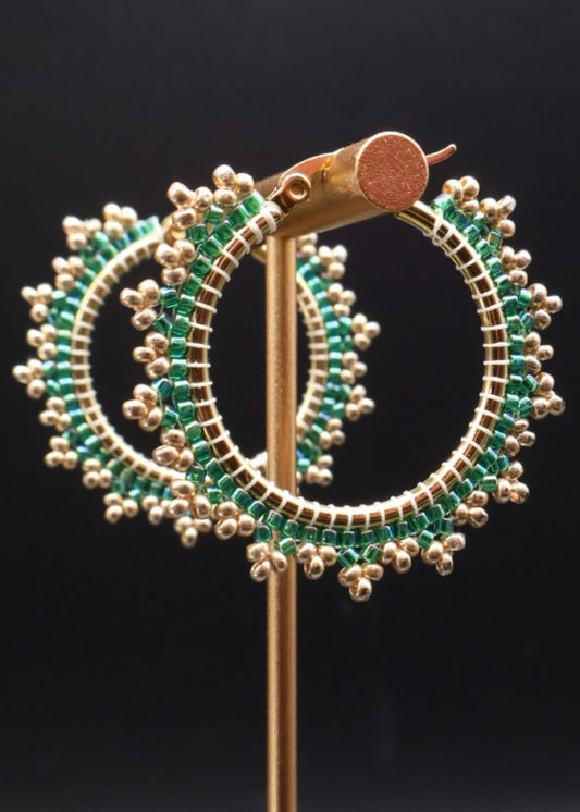 Gold hoop earrings with green gemstones on a black background