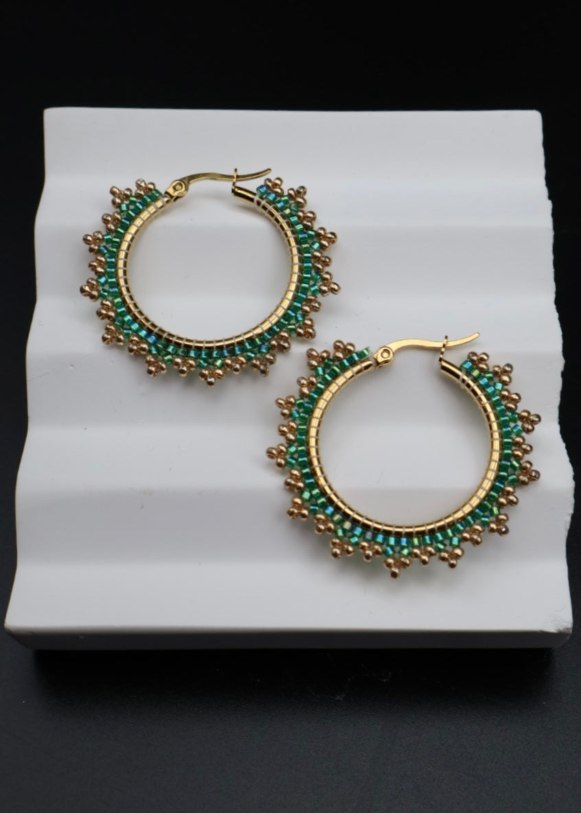 Gold hoop earrings with green gemstones on a white stand against a black background
