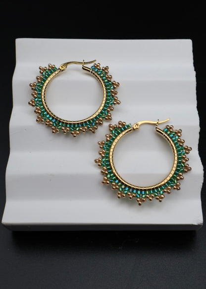 Gold hoop earrings with green gemstones on a white stand against a black background