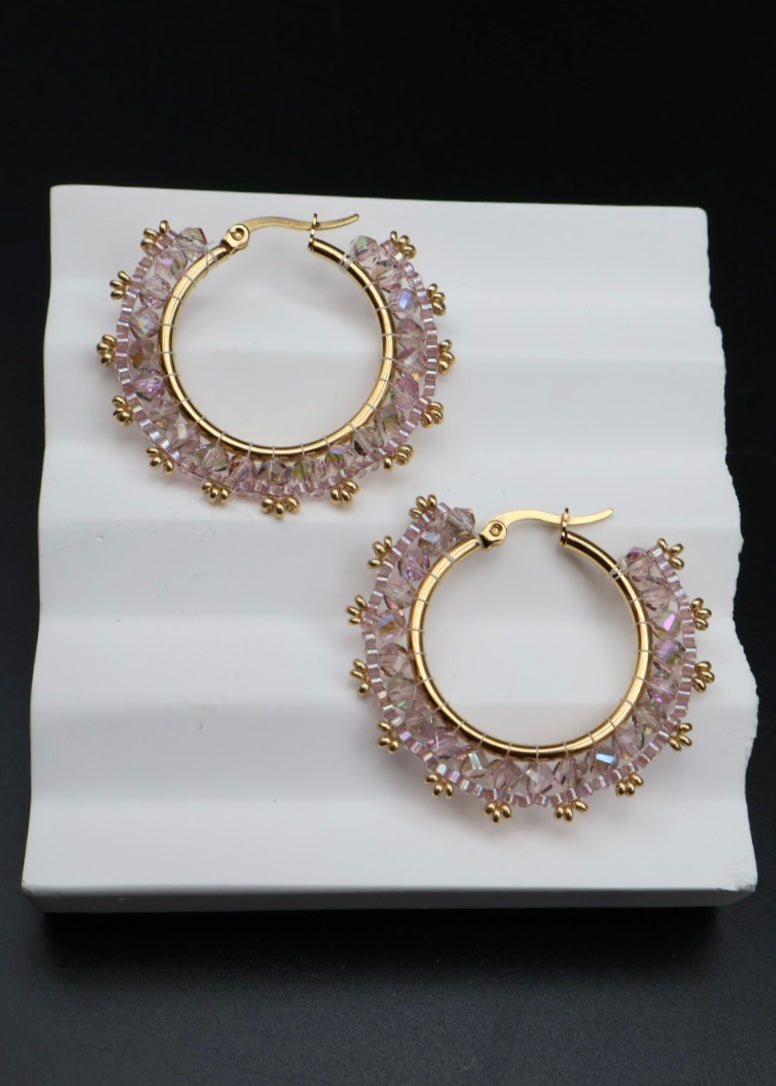 Gold hoop earrings with pink gemstones on a white stand against a black background