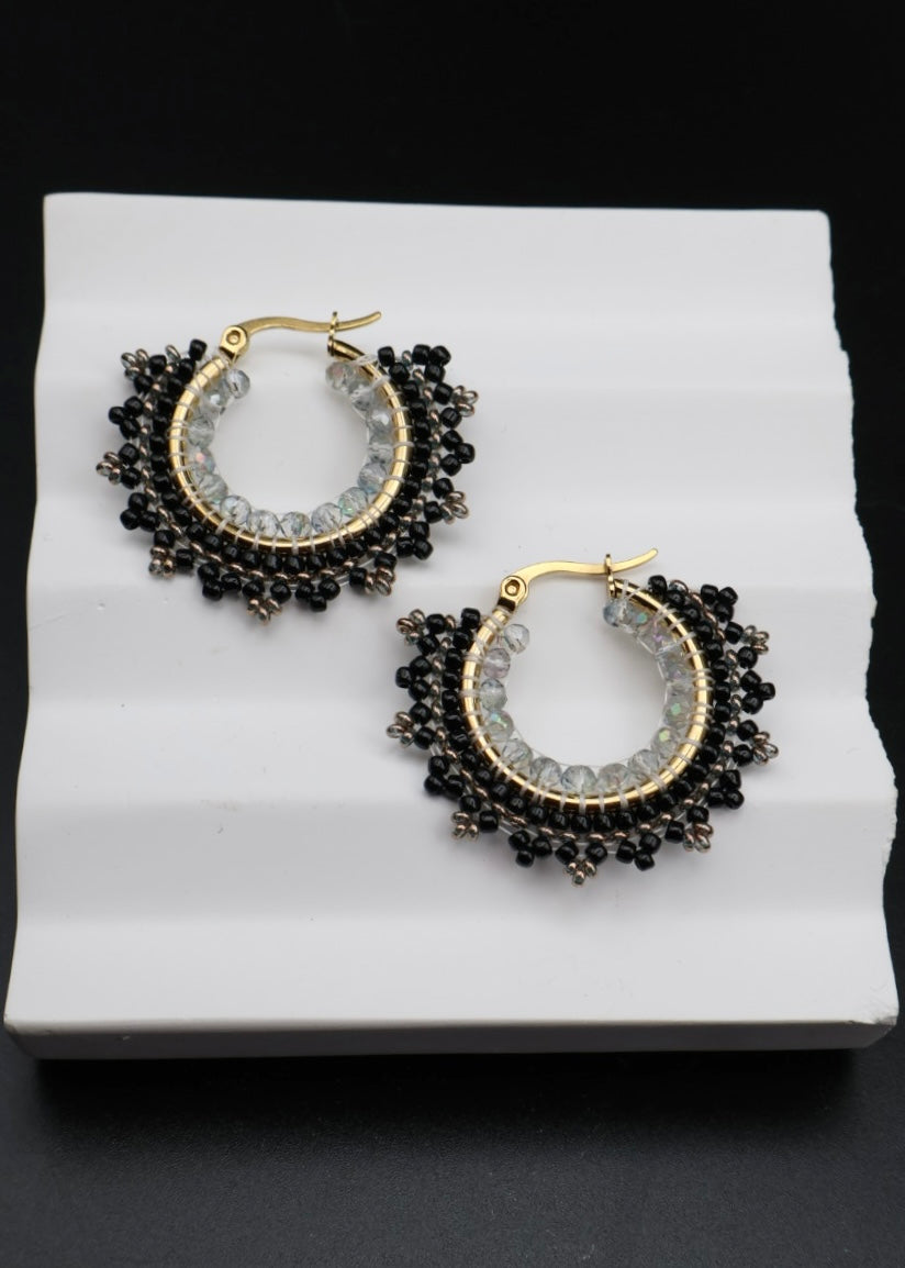 Pair of hoop earrings with black and gold design on a white stand.