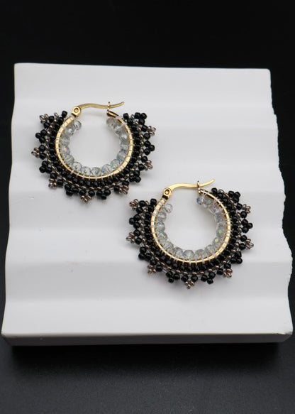 Pair of hoop earrings with black and gold design on a white stand.