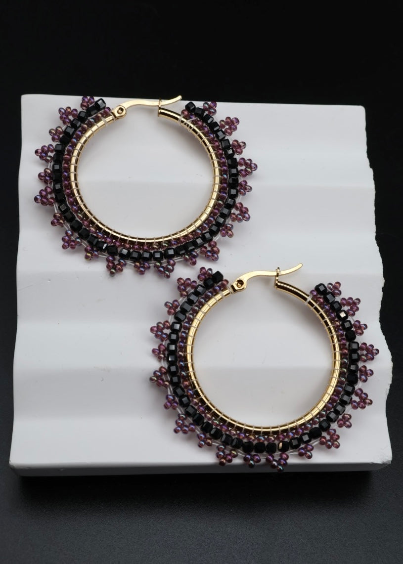 Pair of hoop earrings with purple beads on a white platform against a black background