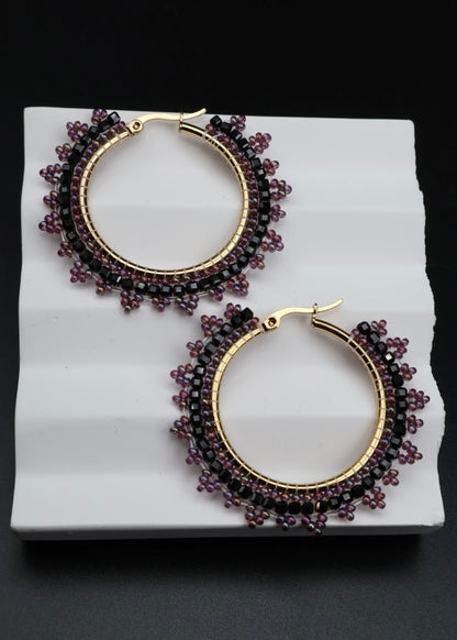 Pair of hoop earrings with purple beads on a white platform against a black background