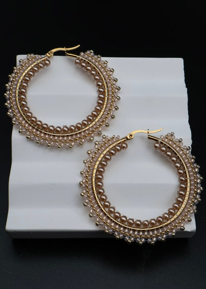 Gold hoop earrings with intricate designs on a white stand against a black background