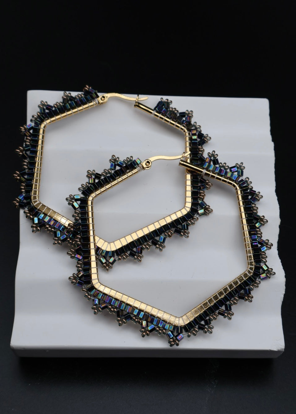 Pair of gold hoop earrings with blue gemstones on a white stand against a black background