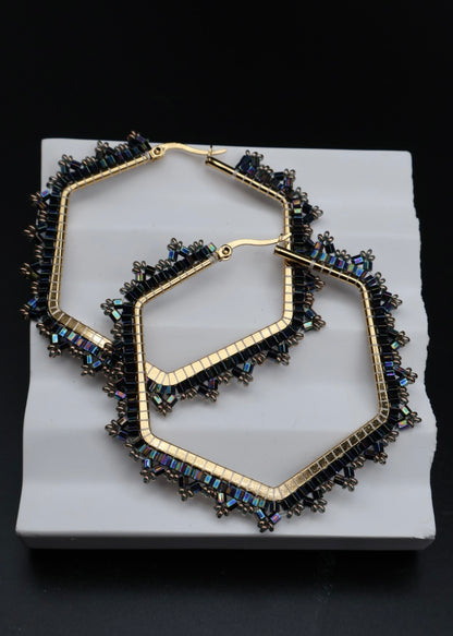 Pair of gold hoop earrings with blue gemstones on a white stand against a black background