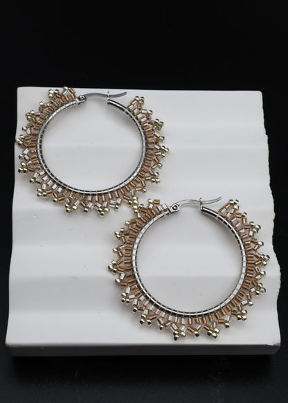 Pair of silver hoop earrings with intricate designs on a white platform.