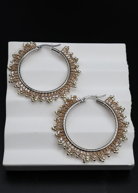 Pair of silver hoop earrings with intricate designs on a white platform.